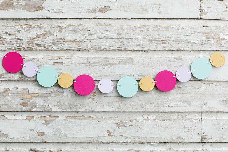 A colorful garland of alternating circles in pink, lavender, mint, and gold hangs against a distressed wooden background.