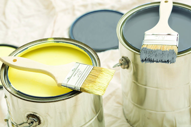 Two open paint cans, one with bright yellow paint and the other with dark gray, each holding a paintbrush.